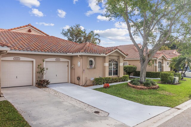 mediterranean / spanish house with a front lawn, driveway, a tiled roof, an attached garage, and stucco siding