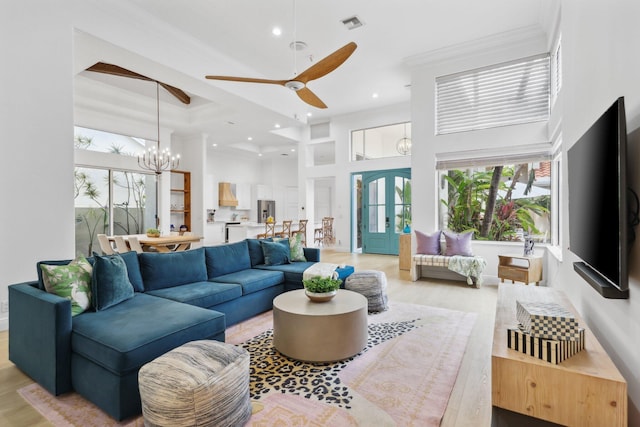 living room with recessed lighting, light wood-style floors, ceiling fan with notable chandelier, a high ceiling, and french doors