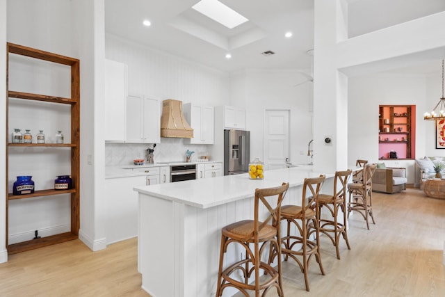 kitchen featuring a kitchen bar, light wood-type flooring, custom range hood, stainless steel appliances, and white cabinets