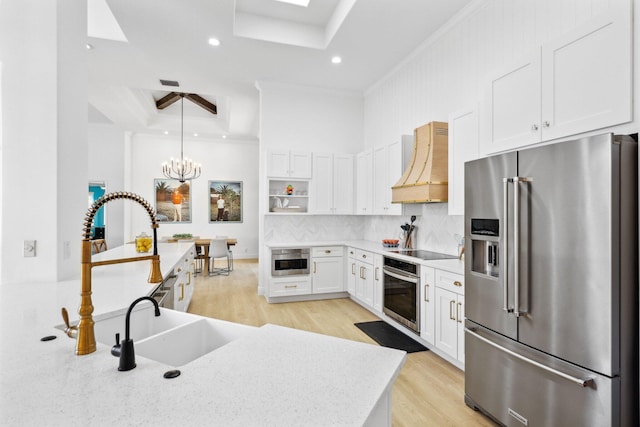kitchen with a sink, a raised ceiling, appliances with stainless steel finishes, custom range hood, and ornamental molding
