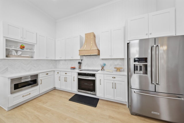 kitchen with light countertops, crown molding, custom range hood, light wood-style flooring, and appliances with stainless steel finishes