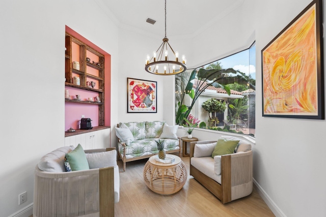living area featuring visible vents, baseboards, ornamental molding, wood finished floors, and an inviting chandelier
