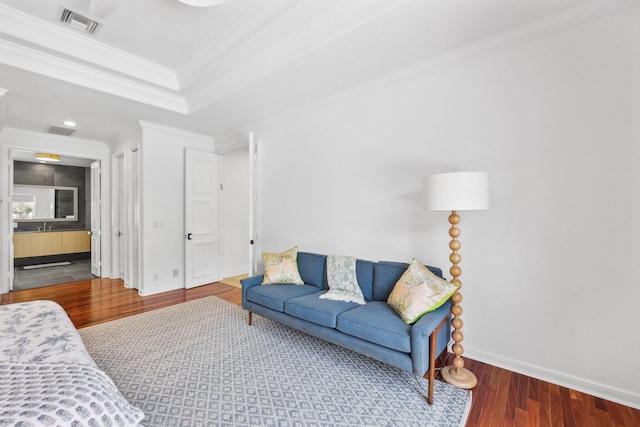 living room with a tray ceiling, wood finished floors, baseboards, visible vents, and ornamental molding