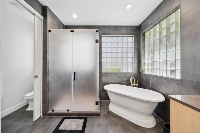 bathroom with tile walls, a shower stall, toilet, a freestanding bath, and tile patterned flooring