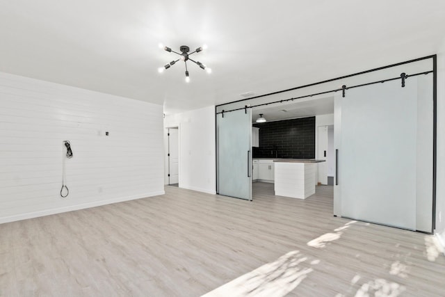 unfurnished living room featuring baseboards, a barn door, and light wood-type flooring