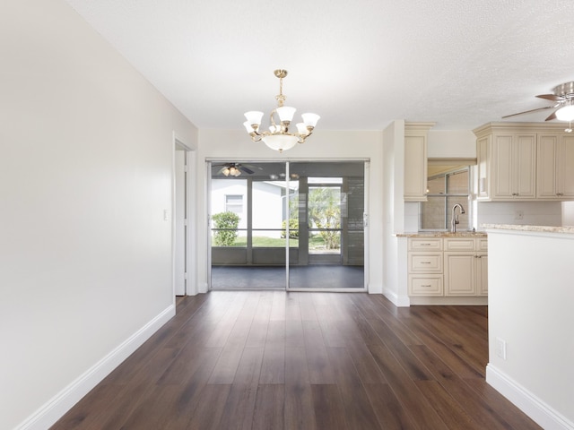 unfurnished dining area with ceiling fan with notable chandelier, baseboards, a textured ceiling, dark wood finished floors, and a sink