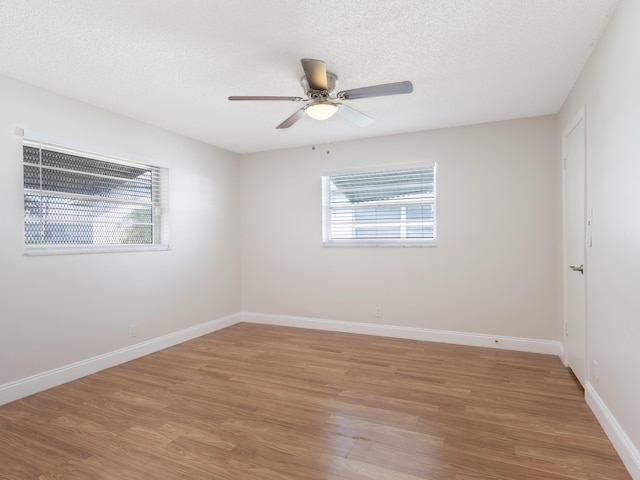 empty room with light wood-style flooring, baseboards, and a textured ceiling