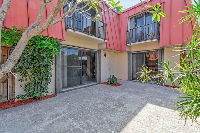 entrance to property featuring a patio, stucco siding, a balcony, and mansard roof