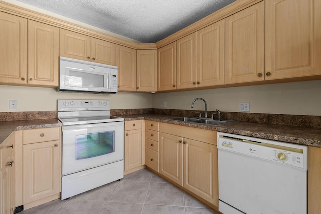 kitchen featuring white appliances, a sink, light brown cabinetry, light tile patterned floors, and dark countertops
