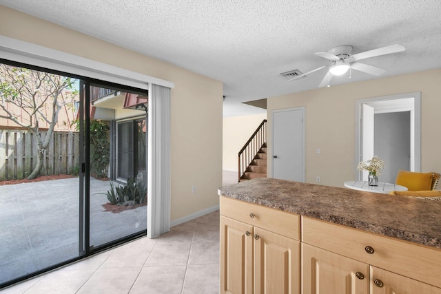 kitchen featuring light brown cabinetry, a ceiling fan, dark countertops, a textured ceiling, and light tile patterned flooring