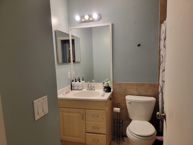 bathroom featuring a wainscoted wall, toilet, vanity, and tile walls
