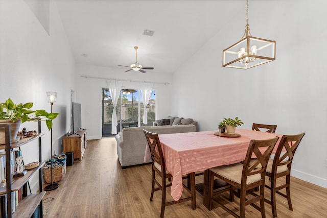 dining room with light wood-type flooring, high vaulted ceiling, ceiling fan with notable chandelier, baseboards, and visible vents