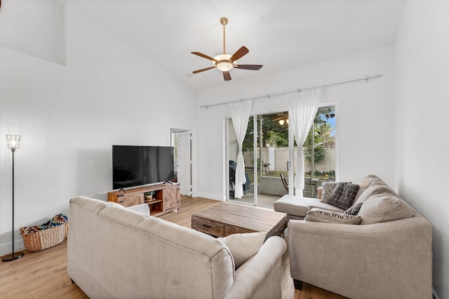 living room featuring a ceiling fan, baseboards, light wood-style floors, and vaulted ceiling