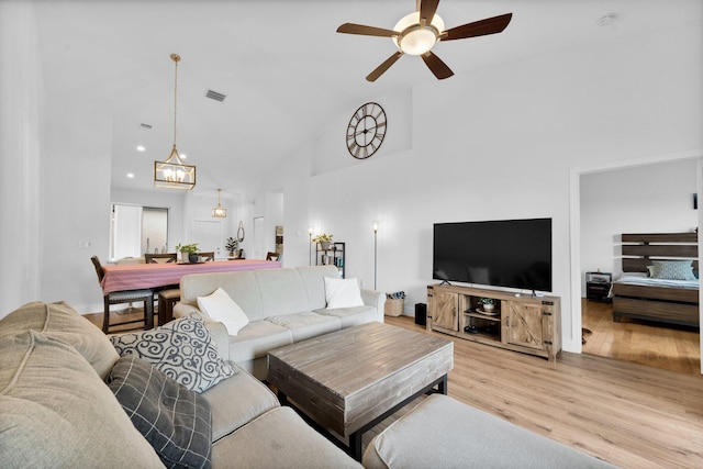 living area featuring high vaulted ceiling, visible vents, wood finished floors, recessed lighting, and ceiling fan with notable chandelier
