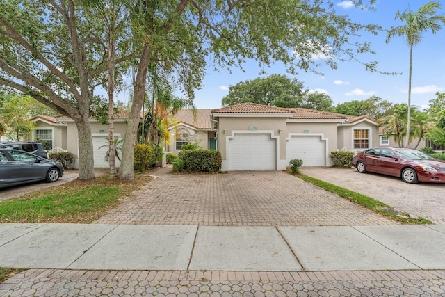 view of front facade with stucco siding, an attached garage, a tile roof, and decorative driveway