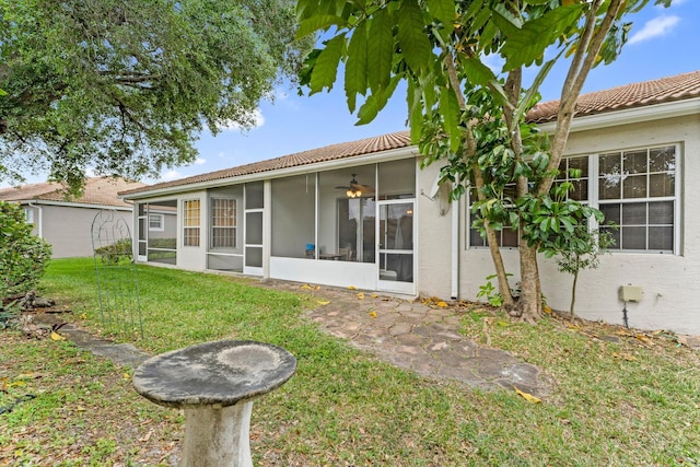 rear view of house with a tile roof, a sunroom, stucco siding, and a lawn
