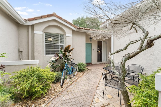 doorway to property with outdoor dining space, a tile roof, stucco siding, and a patio area