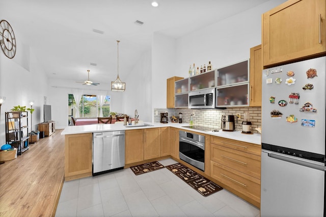 kitchen with light countertops, a peninsula, appliances with stainless steel finishes, a sink, and backsplash