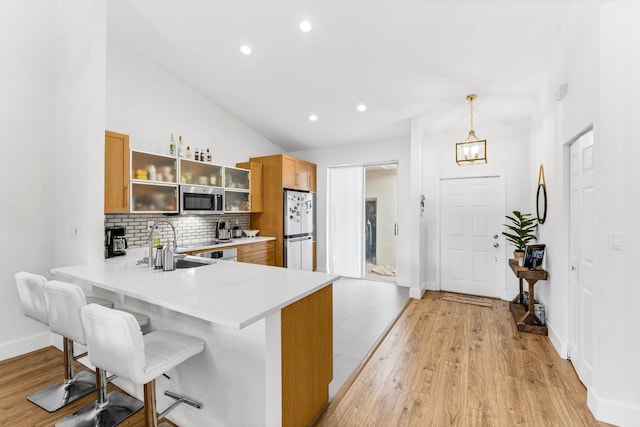 kitchen with freestanding refrigerator, stainless steel microwave, a sink, and light wood-style flooring