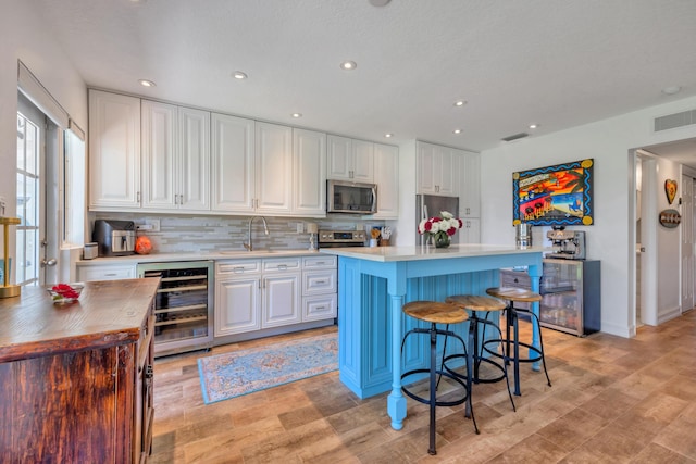 1199 Hillsboro Mile Unit 119, Hillsboro Beach, FL 33062 - kitchen with beverage cooler, white cabinetry, stainless steel appliances, a kitchen bar, and visible vents