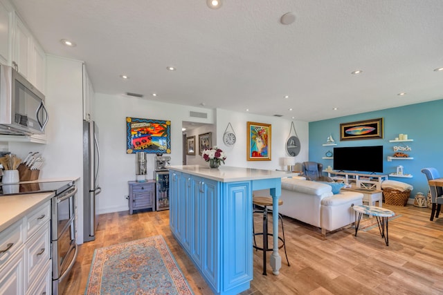 1199 Hillsboro Mile Unit 119, Hillsboro Beach, FL 33062 - kitchen with white cabinets, light wood finished floors, a breakfast bar area, stainless steel appliances, and open floor plan