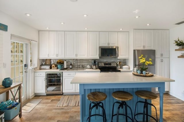 1199 Hillsboro Mile Unit 119, Hillsboro Beach, FL 33062 - kitchen with beverage cooler, white cabinets, tasteful backsplash, light wood-style flooring, and appliances with stainless steel finishes