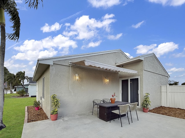 back of house featuring a patio area, a yard, outdoor dining space, fence, and stucco siding