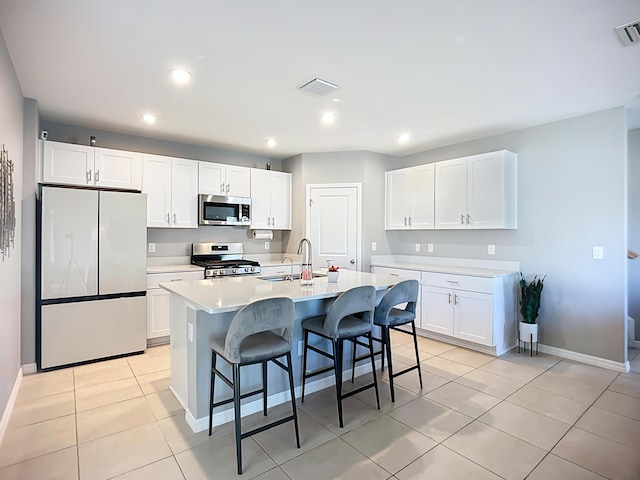 kitchen with a kitchen breakfast bar, a sink, appliances with stainless steel finishes, light countertops, and light tile patterned floors