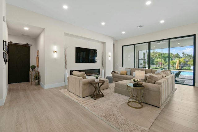 living room with light wood-type flooring, baseboards, recessed lighting, and a barn door