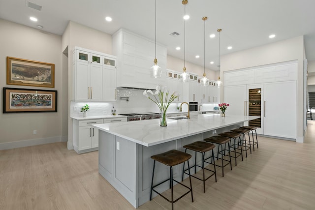 kitchen featuring decorative backsplash, a large island, light wood-style flooring, white cabinets, and visible vents