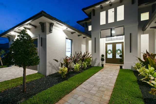 exterior entry at twilight featuring french doors and stucco siding