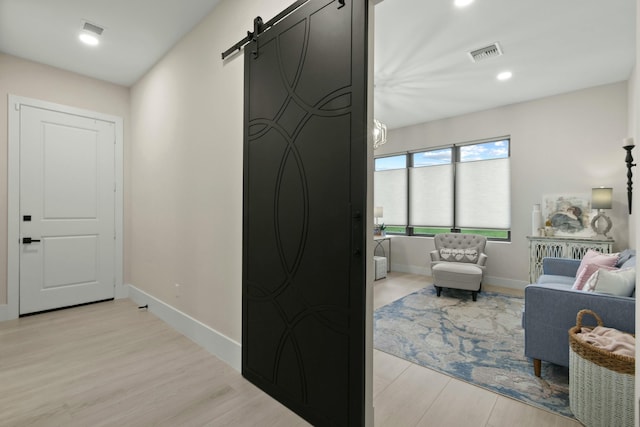 corridor featuring a barn door, baseboards, visible vents, and light wood-style flooring