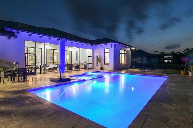 pool at night with a pool with connected hot tub and a patio