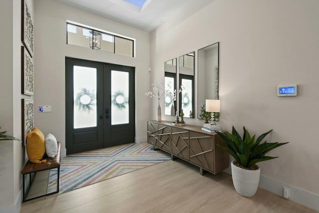 entrance foyer with light wood-type flooring, a high ceiling, baseboards, and french doors