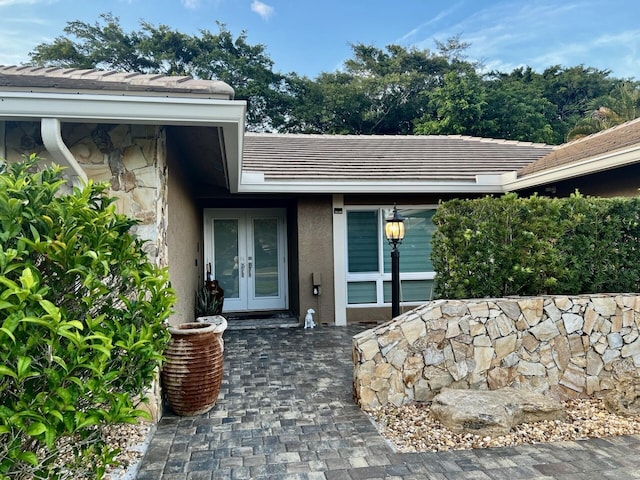 entrance to property with french doors, stone siding, stucco siding, and a tiled roof