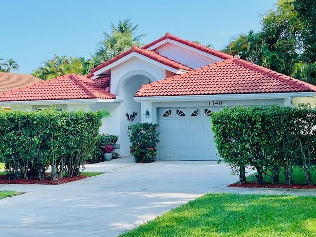 mediterranean / spanish house featuring a tile roof, stucco siding, an attached garage, and driveway