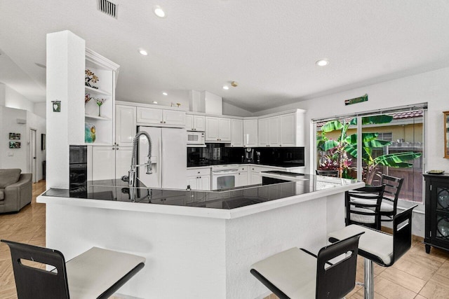 kitchen with white cabinets, a kitchen bar, vaulted ceiling, and white appliances