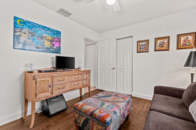 living room featuring baseboards, dark wood finished floors, a textured ceiling, ceiling fan, and visible vents
