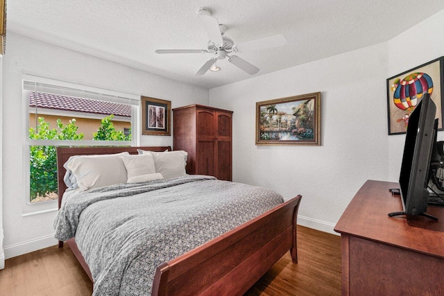 bedroom featuring a ceiling fan, a textured ceiling, baseboards, and wood finished floors