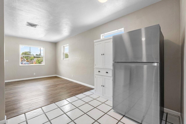 kitchen featuring baseboards, a textured ceiling, light wood finished floors, visible vents, and freestanding refrigerator
