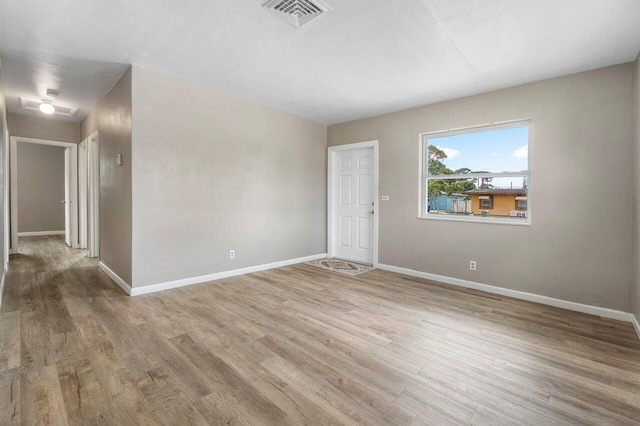 empty room featuring wood finished floors, baseboards, and visible vents