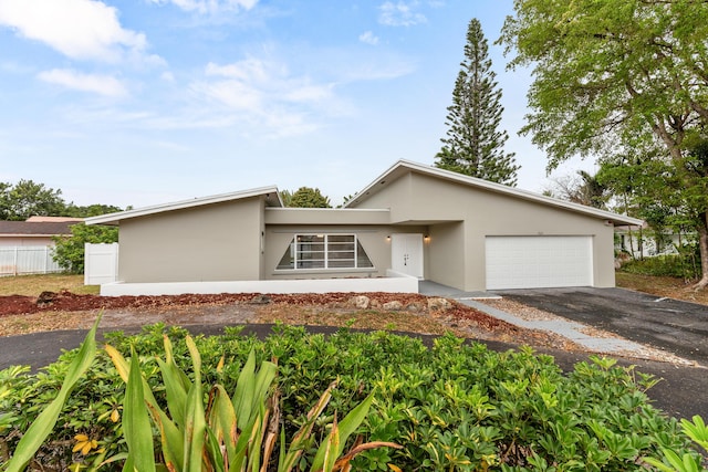 mid-century modern home featuring stucco siding, an attached garage, fence, and aphalt driveway