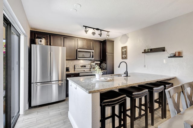 kitchen with light stone counters, dark brown cabinetry, a sink, a peninsula, and stainless steel appliances
