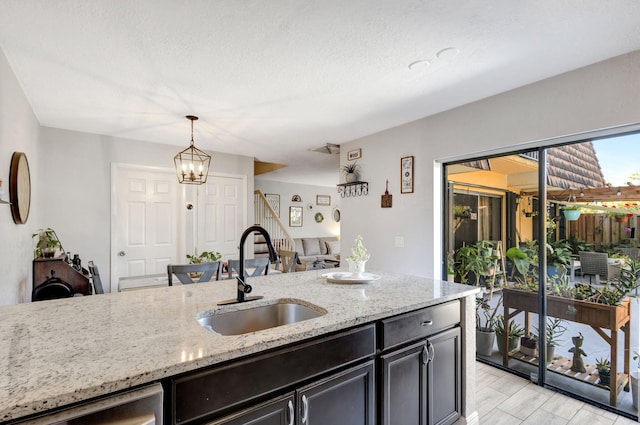 kitchen with light stone counters, a sink, pendant lighting, a textured ceiling, and light wood-style floors