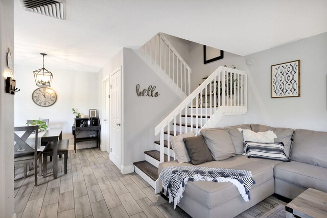 living area featuring stairs, baseboards, a chandelier, light wood-style floors, and visible vents