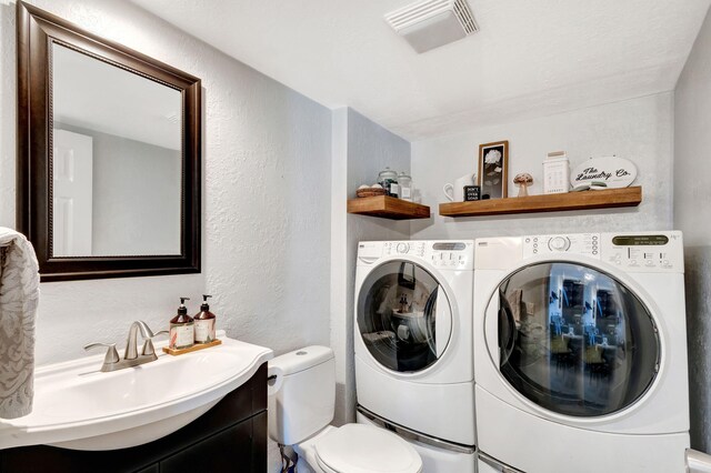 clothes washing area with washer and clothes dryer, a sink, laundry area, visible vents, and a textured wall