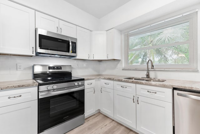 kitchen with light wood-style flooring, appliances with stainless steel finishes, white cabinetry, a sink, and backsplash