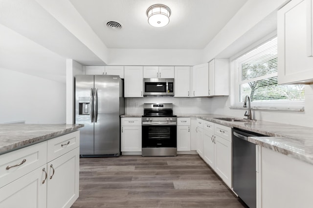 kitchen with white cabinetry, stainless steel appliances, a sink, visible vents, and wood finished floors