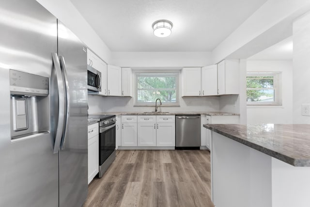 kitchen featuring stainless steel appliances, dark stone counters, a sink, light wood-style floors, and white cabinets