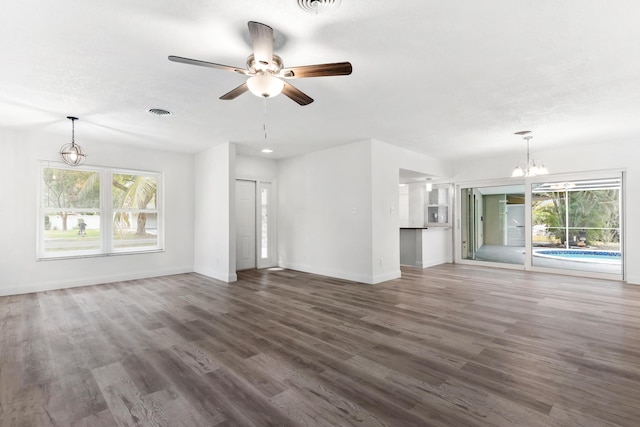 unfurnished living room featuring baseboards, wood finished floors, a healthy amount of sunlight, and ceiling fan with notable chandelier